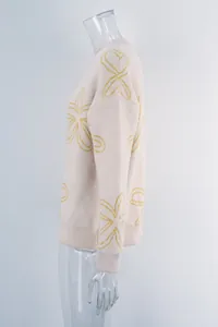 Detail shot of cream floral knit sweater with yellow flower patterns and ribbed cuffs.
