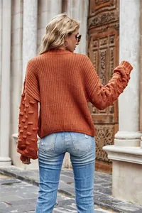 Detailed rear view of burnt orange knitted sweater featuring pom-pom textured sleeves