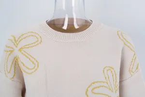 Macro view of cream knitted sweater featuring yellow floral line art and ribbed neckline
