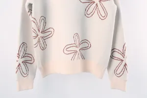 Detail view of white knitted sweater with brown flower pattern and ribbed hem