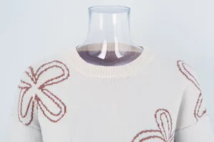 Detailed view of cream knitted sweater featuring brown floral outlines and ribbed collar