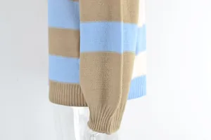 Close-up of striped knit sweater showing ribbed cuff and blue/tan color blocking.