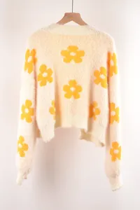 Detalle del jersey de punto suave color crema con motivos de flores amarillas y textura blanda