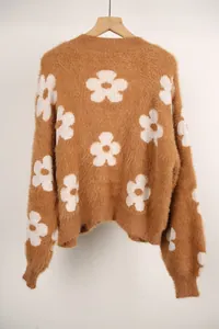 Suéter de punto marrón suave con grandes motivos florales blancos en una percha de madera.