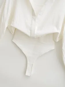 Detail of white ribbed long-sleeve shirt bodysuit showing button front and bottom closure
