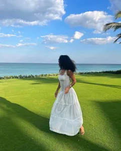 Elegante vestido largo blanco con volantes estilo resort en un césped junto al mar azul