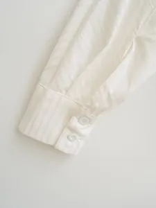 Close-up view of a white shirt cuff featuring striped texture and double buttons