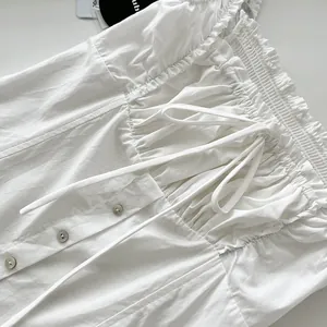 Detalle de vestido blanco con volantes, botones delanteros y cordón ajustable.
