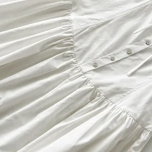 Detalle de un vestido largo plisado blanco con botones y cordón delicado.