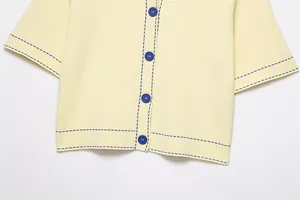 Détail d'un chemisier en tricot crème avec surpiqûres et boutons bleus contrastés