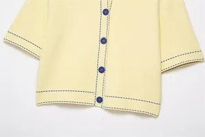 Detailed close-up of a pale yellow knit cardigan with contrast navy blue stitching and buttons