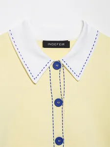 Détail d'un haut polo en maille jaune avec col blanc et surpiqûres bleues élégantes.