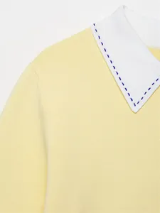 Close-up detail of yellow knit polo sweater with white collar and blue decorative stitching.