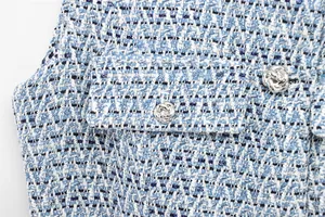 Gros plan d'un gilet en tweed bleu avec fils métalliques et bouton rose argenté