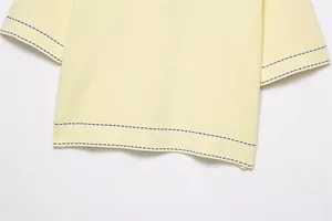 Détail macro d'un pull en maille jaune pâle avec coutures contrastées bleues à l'ourlet