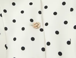 Détail en gros plan d'un blazer blanc à pois avec bouton doré décoratif