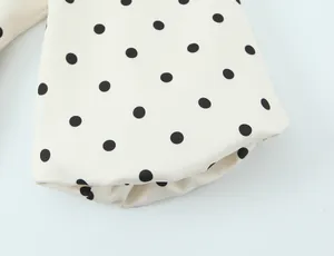 Gros plan détaillé sur la manche d'un blazer crème à pois noirs avec un revers soigné.