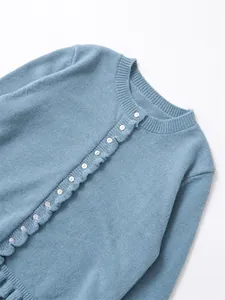 Detail view of blue crew neck knitted cardigan featuring ruffle trim and white buttons.