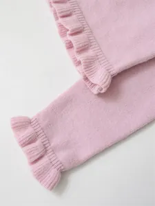 Close-up detail of soft pink knit sweater sleeve with delicate ruffled cuff design