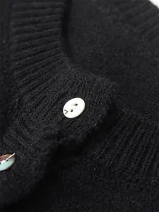 Detail shot of black knitted sweater with ribbed neckline and white button accent.