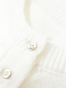Macro detail of white knit cardigan neckline featuring elegant pearlescent buttons