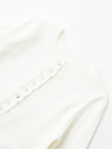 Close-up detail of a white knitted cardigan with shell buttons and ribbed round neckline