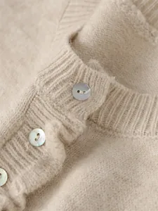Macro detail of soft beige knit sweater showing ribbed collar and iridescent buttons