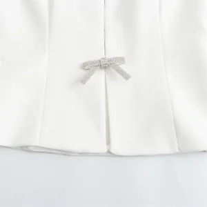 Close-up of sparkling rhinestone bow-knot detail on a white halter-neck fashion top