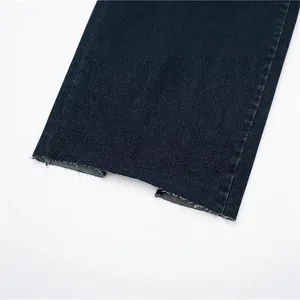 Dettaglio dell'orlo a taglio vivo con spacco su un abito di jeans blu scuro da donna.