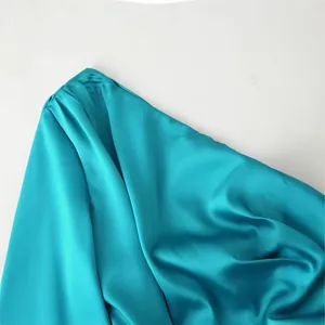 Close-up detail of peacock blue satin one-shoulder dress with ruffled sleeve texture