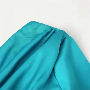 Close-up of elegant teal satin one-shoulder dress showing intricate ruffled drapery detail