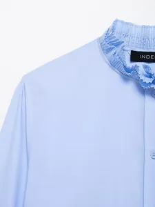 Detailopname van een lichtblauwe blouse met een gerimpelde opstaande kraag en knopen.
