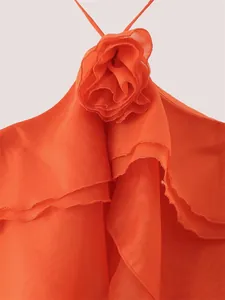 Détail d'une fleur en tissu 3D orange et de volants superposés sur une robe d'été