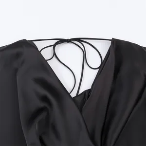 Close-up detail of black silk satin dress showing elegant draped neckline and thin strap tie