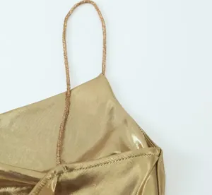 Close-up detail of a shiny metallic gold slip dress featuring a delicate spaghetti strap.