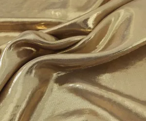 Close-up of shimmering gold metallic fabric texture with elegant draped folds for dress