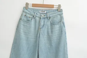 Detail of light blue low-waist denim jeans featuring metal button and front pockets