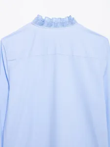 Gedetailleerde weergave van de geplooide ruffelkraag op een lichtblauwe damesblouse