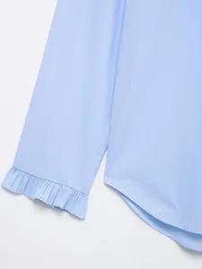 Detail van lichtblauwe blouse met geplooide ruches aan de manchetten en ronde zoom.