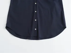 Close-up detail of dark navy satin texture shirt with white buttons and curved hem.