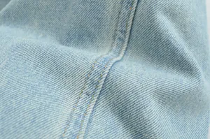 Detailed close-up of light blue denim fabric with yellow contrast stitching texture.