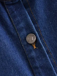 Macro detail of blue denim fabric with a vintage metal button featuring a heart engraving