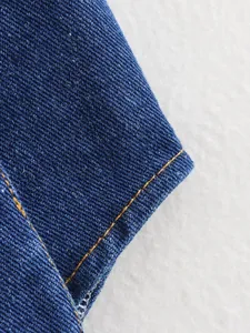 Macro view of blue denim fabric with orange stitching details on a white background.