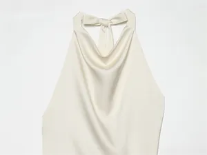 Primer plano del top de seda crema con cuello halter, lazo y elegante escote drapeado.