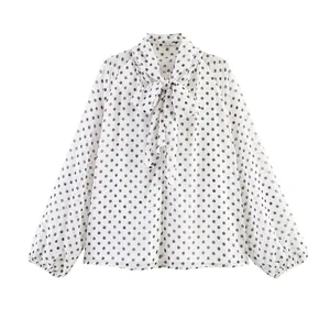 Close-up of white long-sleeved blouse with black polka dots and a stylish bow tie collar