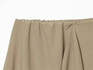 Close-up detail of the elastic waistband and khaki fabric drape of an asymmetric skirt