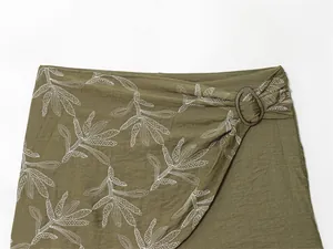 Close-up detail of olive green wrap garment featuring white leaf embroidery and ring buckle