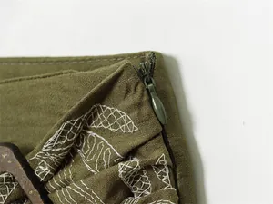 Detailed macro view of olive green garment with white embroidery and side invisible zipper