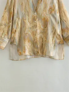 Macro detail of tie-dye marble print satin shirt with high-low hem and side slits.