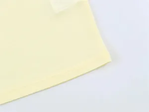 Dettaglio ravvicinato dell'orlo con doppia cucitura di una polo a maniche lunghe giallo chiaro.